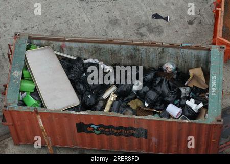 Orangefarbener, oben offener Behälter voller Müll in schwarzen Plastiktüten am Pier im Hafen von Kapstadt. Stockfoto