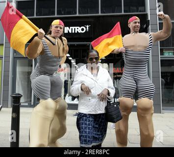 Manchester, Vereinigtes Königreich, 29. Juli 2023. Retro-Rettungsschwimmer mit altmodischen Badeanzügen und Flaggen bieten an, mit Passanten zu posieren, um Fotos und Selfies auf Deansgate neben dem Manchester Airport zu machen. Manchester Day - im Urlaub!, kostenlos, Spaß, familienfreundlich, Veranstaltungen in den Straßen des Stadtzentrums von Manchester, Großbritannien. Unterstützt von Manchester City Council, Manchester Airport Group, Biffa, The Co-op, Manchester Evening News, Wandern Sie auf dem Plank, Kingdom of Sweets, British Firefighter Challenge und Capri Beach Club. Kredit: Terry Waller/Alamy Live News Stockfoto