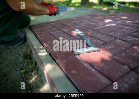 Der Winkelmesser liegt auf den Pflastersteinen und der Arbeiter legt den Bürgersteig. Stockfoto