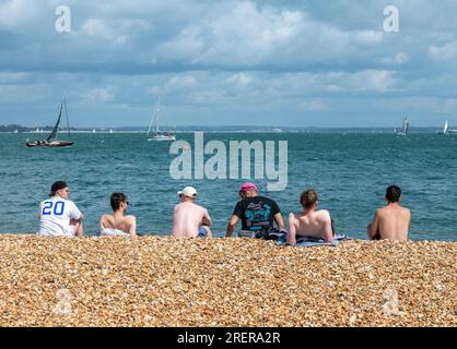 Gruppe von Jungs, die zusammen am Strand an einem heißen, sonnigen Tag im cowes auf der Insel wight uk sitzen Stockfoto