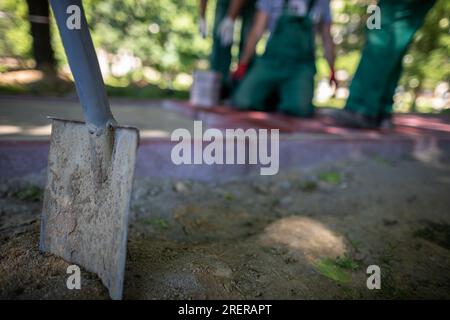 Im Vordergrund, eine Schaufel im Boden und Bauarbeiter im Hintergrund. Stockfoto