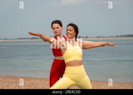 Yoga-Kurse im Freien an der Küste. Lehrer, der Klient hilft. Küstenlage. Stockfoto