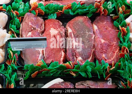 Ein Ribeye-Steak wird auf einem schwarzen Tablett serviert und ist in einer Metzgerei mit Essensdekorationen geschmückt. Stockfoto