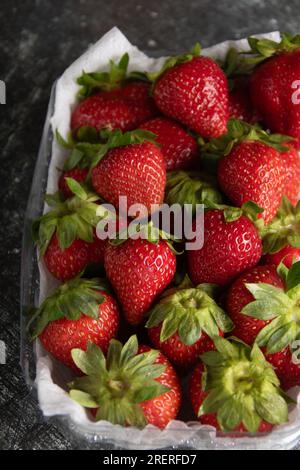 Fotosaftige, frische, reife Erdbeeren in einem Kunststoffbehälter, Draufsicht, vertikales Foto Stockfoto