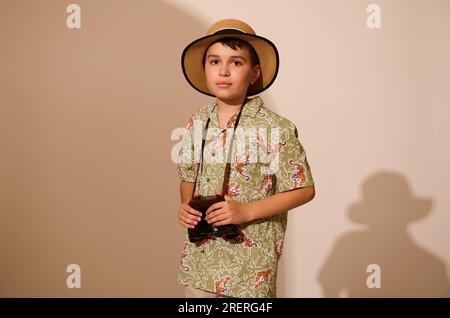 Ein hübscher lateinamerikanischer Teenager in stilvoller, lässiger Sommerkleidung und Strohhut, ein glücklicher Touristenabenteuer, der ein Fernglas in der Hand hält, sieht aus wie ein C Stockfoto