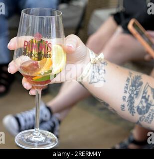 Manchester, Vereinigtes Königreich, 29. Juli 2023. Eine Person mit Armtätowierungen hält ein Getränk in einem Pimms Glas in der Pop-up Capri Beach Bar, Exchange Square, Manchester, UK. Manchester Day - im Urlaub!, kostenlos, Spaß, familienfreundlich, Veranstaltungen in den Straßen des Stadtzentrums von Manchester, Großbritannien. Unterstützt von Manchester City Council, Manchester Airport Group, Biffa, The Co-op, Manchester Evening News, Wandern Sie auf dem Plank, Kingdom of Sweets, British Firefighter Challenge und Capri Beach Club. Kredit: Terry Waller/Alamy Live News Stockfoto