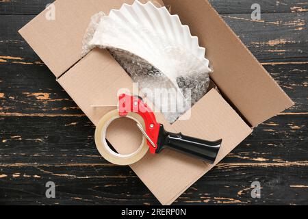 Abroller für Verpackungsband und Karton auf schwarzem Holzhintergrund Stockfoto