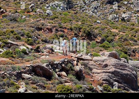 Junges Paar auf dem Weg von Livadia zum Strand von Lethra entlang des felsigen Bergpfads, Insel Tilos, Inselgruppe Dodekanes. Griechenland, Juli 2023 Stockfoto