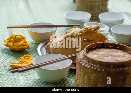 Ein traditionell gekochtes vietnamesisches Hähnchengericht, umgeben von kleinen Schüsseln, Hackstäbchen und einem Korb mit frisch gekochtem Reis Stockfoto