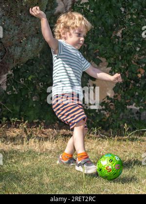 Ein kleiner Junge tritt einen Ball im Sommergarten Stockfoto