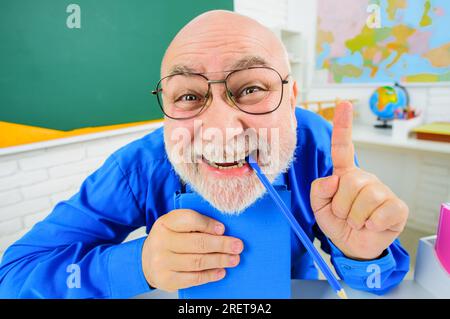 Zurück in die Schule. Lustige Lehrerin mit Notizbuch, das mit dem Finger nach oben zeigt. Glücklicher Lehrer in Brille mit Copybook im Klassenzimmer. Lehrertag. Professor Giving Stockfoto