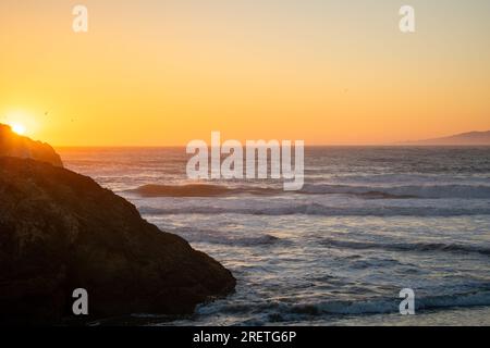 Ruhiger Sonnenuntergang über dem ruhigen Ozean, der ein goldenes Leuchten ausstrahlt. Stockfoto