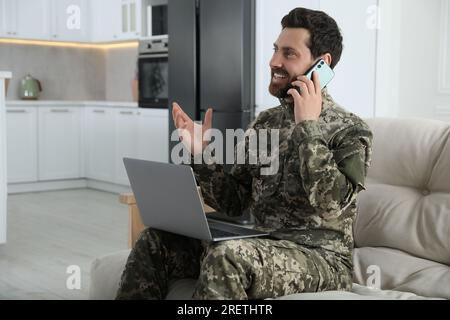 Glücklicher Soldat mit Laptop, der zu Hause telefoniert. Militärdienst Stockfoto