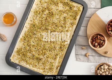 Ich mache köstliche Baklava. Backpfanne mit Teig und Zutaten auf weißem Holztisch, flach liegend Stockfoto