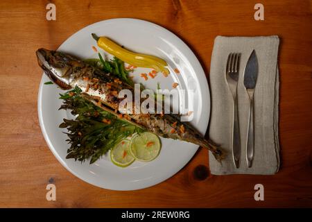 Gegrillte Makrele mit Chili, Limette und Koriander auf einem weißen Teller mit Besteck Stockfoto