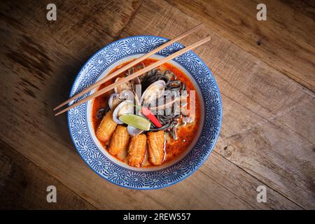 Typisch scharfes Ramen-Gericht mit Fischbrühe in einer Schüssel mit schwarzen Nudeln, Tintenfisch, Chili, Muscheln. Stockfoto