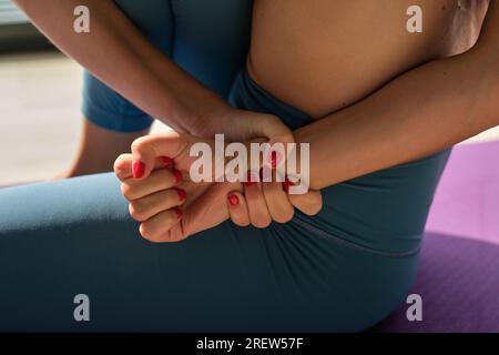 Hoher Erntegutwinkel, nicht erkennbare Frau in Sportbekleidung, die beim Training von Marichyasana während der Yoga-Session die Hände umschließt Stockfoto
