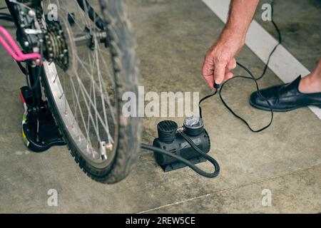 Von oben: Anonymer Seniorenfahrrad mit Elektrowerkzeug und Manometer aufblasen Stockfoto