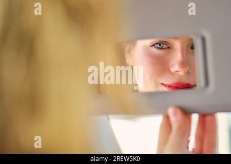 Crop Attraktive weibliche tragen leuchtend roten Lippenstift Blick in Eitelkeit Spiegel auf Sonnenblende, während im Auto sitzen Stockfoto