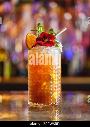 Glas mit alkoholischen Cocktails, dekoriert mit Blumen und getrockneten Orangen, serviert an der Theke auf verschwommenem Hintergrund mit Bokeh Stockfoto