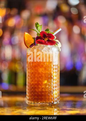 Ein Glas Longdrink-Cocktail mit Eiswürfeln und Dekorationen, serviert an der Theke in einer modernen Bar auf verschwommenem Hintergrund mit Bokeh Stockfoto