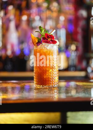 Alkoholische Longdrink-Cocktails mit Blumen- und Orangenscheiben, serviert mit Stroh auf der Theke vor verschwommenem Hintergrund Stockfoto