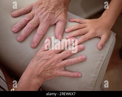 Von oben Hände von anonymen Großeltern und Kind auf der Armlehne der bequemen Couch im hellen Wohnzimmer zu Hause Stockfoto