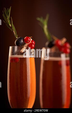 Gläser mit Champagner, dekoriert mit roten Johannisbeeren und schwarzen Johannisbeeren, serviert mit grünen Rosmarin-Zweigen im Zimmer während der festlichen Veranstaltung Stockfoto