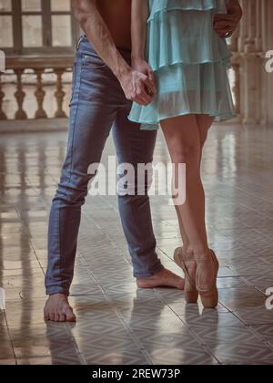 Baue unbekannte Ballerina und männliche Balletttänzerin in Denim auf, die Hand halten, während sie zusammen auf dem gefliesten Boden stehen Stockfoto