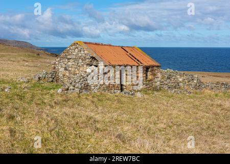 Ein kleines Steingebäude mit einem rostigen Metalldach am ruhigen blauen Meer an der Westküste Schottlands Stockfoto