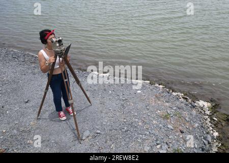 Hübsche asiatische Vermessungsfrau oder Ingenieurin, die mit Theodolith-Transitgeräten auf einer Baustelle im Freien arbeitet. Stockfoto