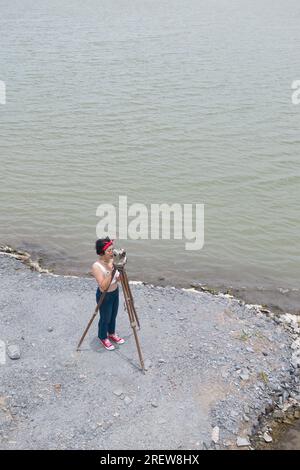 Hübsche asiatische Vermessungsfrau oder Ingenieurin, die mit Theodolith-Transitgeräten auf einer Baustelle im Freien arbeitet. Stockfoto