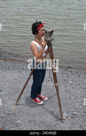 Hübsche asiatische Vermessungsfrau oder Ingenieurin, die mit Theodolith-Transitgeräten auf einer Baustelle im Freien arbeitet. Stockfoto