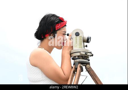 Hübsche asiatische Vermessungsfrau oder Ingenieurin, die mit Theodolith-Transitgeräten auf einer Baustelle im Freien arbeitet. Stockfoto