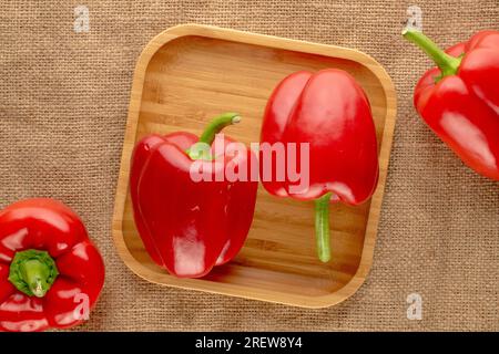 Vier süße rote Paprika mit Bambusschale auf Jutetuch, Makro, Draufsicht. Stockfoto