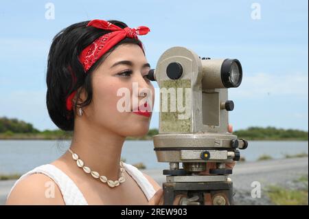 Hübsche asiatische Vermessungsfrau oder Ingenieurin, die mit Theodolith-Transitgeräten auf einer Baustelle im Freien arbeitet. Stockfoto