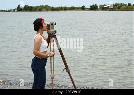 Hübsche asiatische Vermessungsfrau oder Ingenieurin, die mit Theodolith-Transitgeräten auf einer Baustelle im Freien arbeitet. Stockfoto