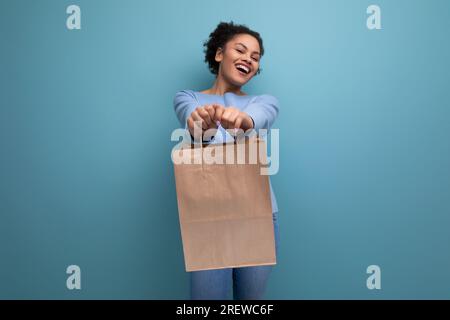 Positive brünette Afro-haarige Frau bekam eine Lieferung in einem Handwerkspaket Stockfoto