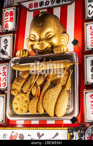 Großes Skulpturenschild mit einem Mann, der einen Grill mit beschichteten Fischstücken über dem Eingang des Teppan Jinja Restaurants in Dotonbori, Osaka hält. Stockfoto