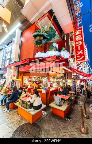 Das sehr beliebte Restaurant Kinryu Ramen in Dotonbori, Osaka. Die Gäste sitzen an kleinen Tischen vor der Theke und essen abends Nudeln. Stockfoto