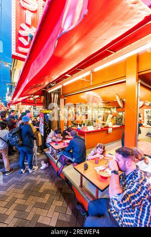 Das sehr beliebte Restaurant Kinryu Ramen in Dotonbori, Osaka. Die Gäste sitzen an kleinen Tischen vor der Theke und essen abends Nudeln. Stockfoto