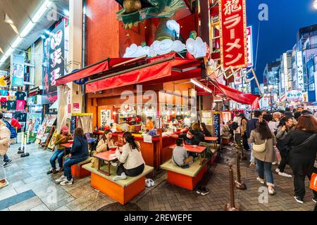 Das sehr beliebte Restaurant Kinryu Ramen in Dotonbori, Osaka. Die Gäste sitzen an kleinen Tischen vor der Theke und essen abends Nudeln. Stockfoto