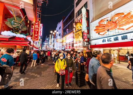 Nachtsicht entlang der belebten Dotonbori Straße mit dem beliebten Kani Doraku Seafood Restaurant mit seiner großen mechanischen Krabbe über dem Eingang. Stockfoto