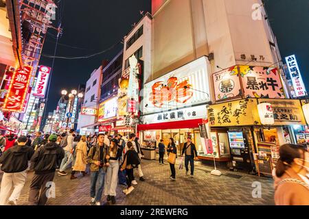 Nachtsicht entlang der belebten Dotonbori Straße mit dem beliebten Kani Doraku Seafood Restaurant mit seiner großen mechanischen Krabbe über dem Eingang. Stockfoto