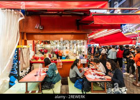 Das sehr beliebte Restaurant Kinryu Ramen in Dotonbori, Osaka. Die Gäste sitzen an kleinen Tischen vor der Theke und essen abends Nudeln. Stockfoto