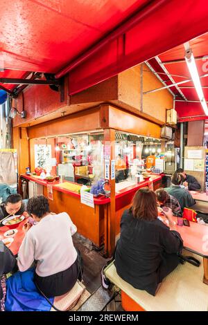 Das sehr beliebte Restaurant Kinryu Ramen in Dotonbori, Osaka. Die Gäste sitzen an kleinen Tischen vor der Theke und essen abends Nudeln. Stockfoto