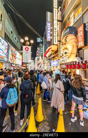 Vor dem Eingang des beliebten Restaurants Kushikatsu daruma mit seinem berühmten, wütenden Chefkoch in Dotonbori, Osaka, warten Schlangen an Leuten. Stockfoto