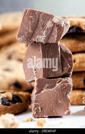 Große Stücke Milchschokolade auf dem Tisch, zerbrochene Schokolade und Weizenkekse mit Schokoladentropfen, Fastfood-Artikel, sehr kalorienreiches Kakaopulver Stockfoto