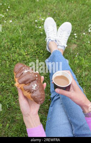 Kaffee in einem Pappbecher und Schokoladen-Croissant in den Händen einer Frau. Vertikal Stockfoto