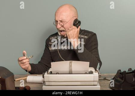 Journalist aus der Vergangenheit bei der Arbeit. Schreibtisch mit Telefon und Schreibmaschine. Vintage-Porträt Stockfoto
